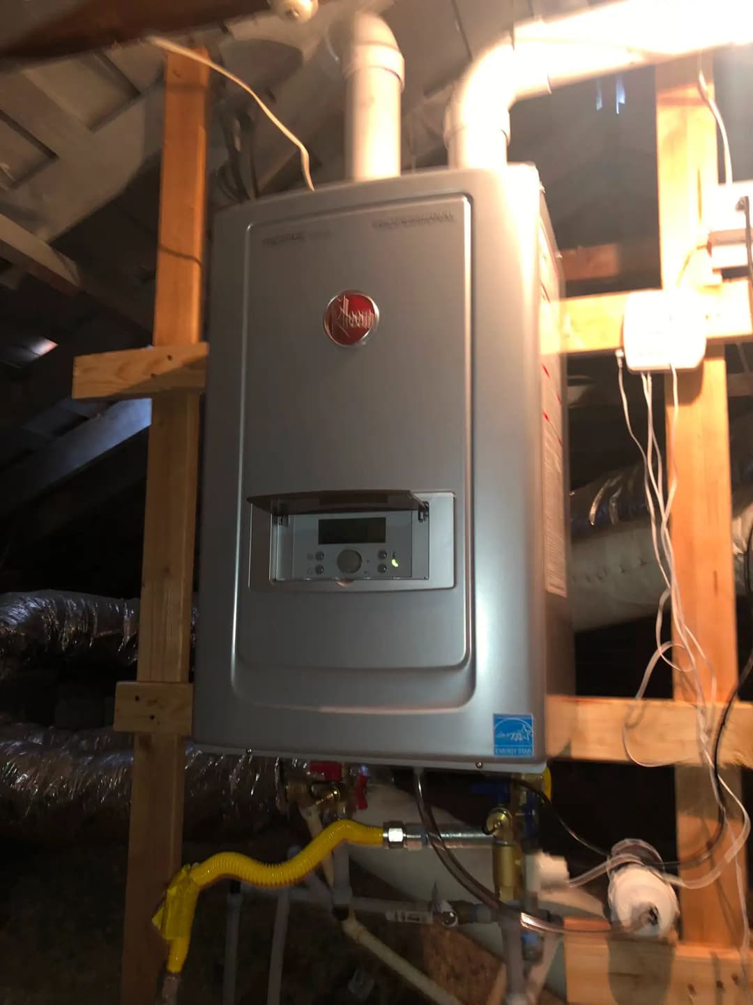 Tankless water heater installation in a home attic with visible plumbing and electrical connections.