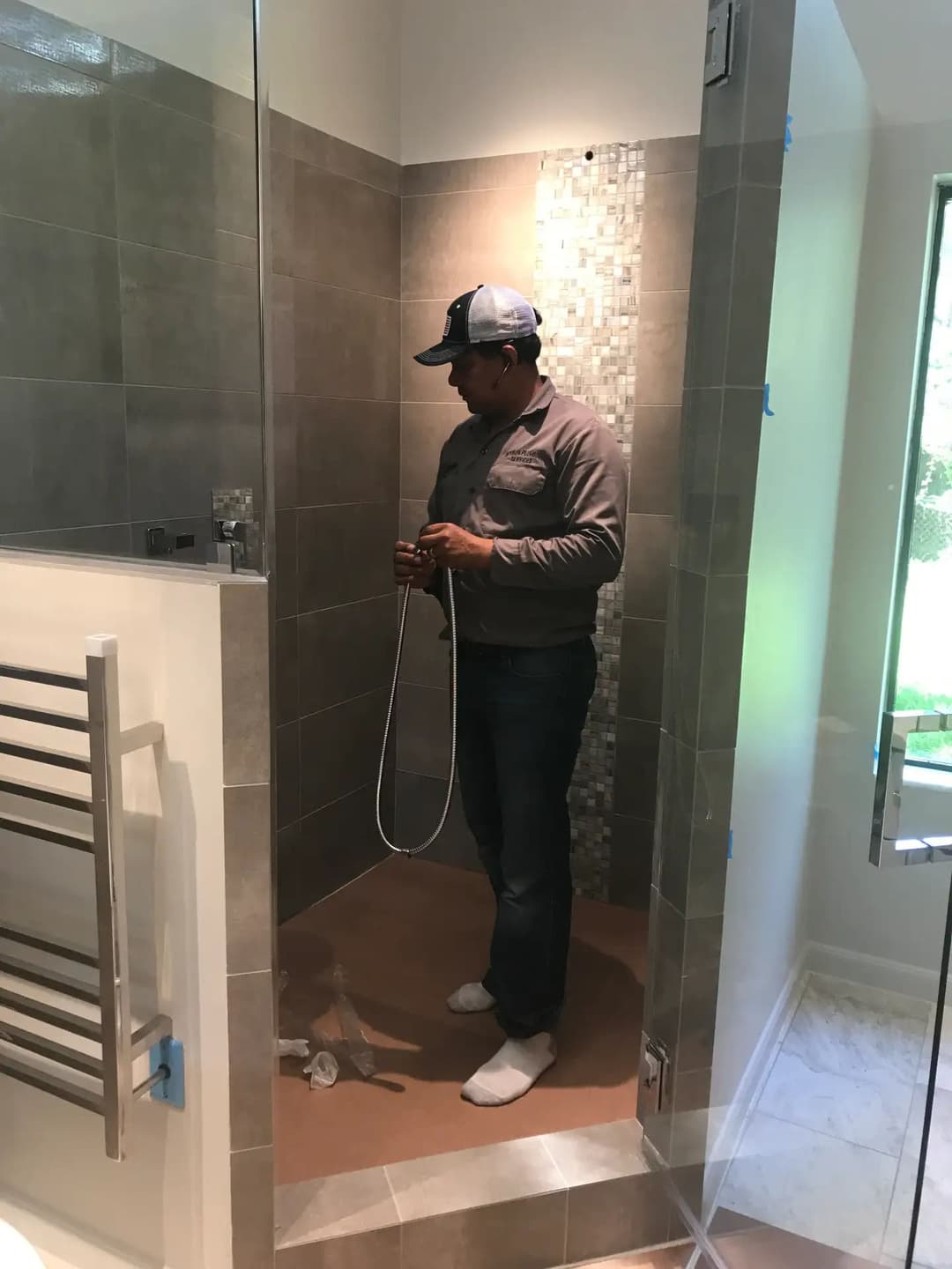 Person installing a shower in a modern bathroom with tile walls and glass enclosure.