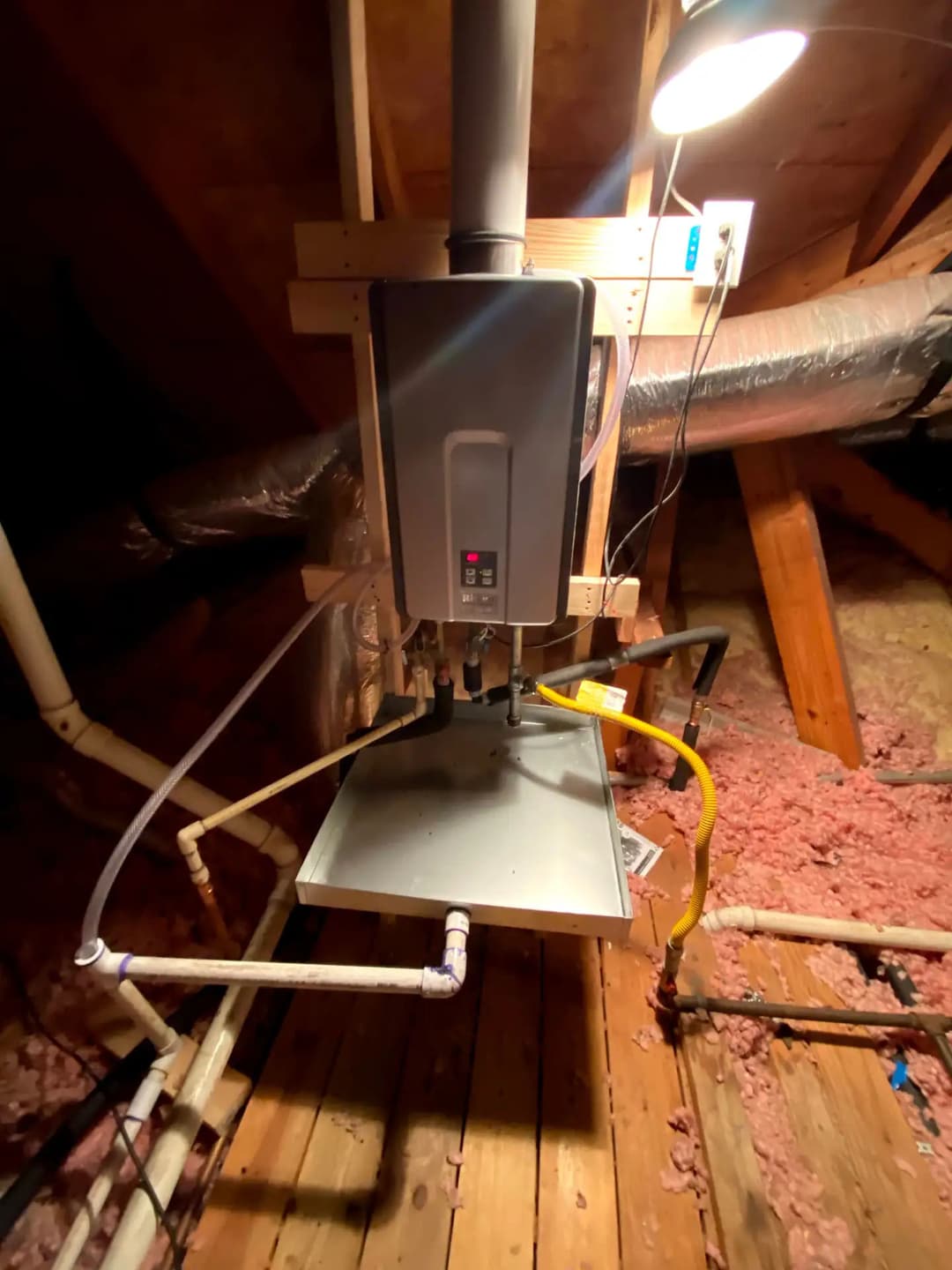 Tankless water heater installation in an attic with exposed pipes and insulation.