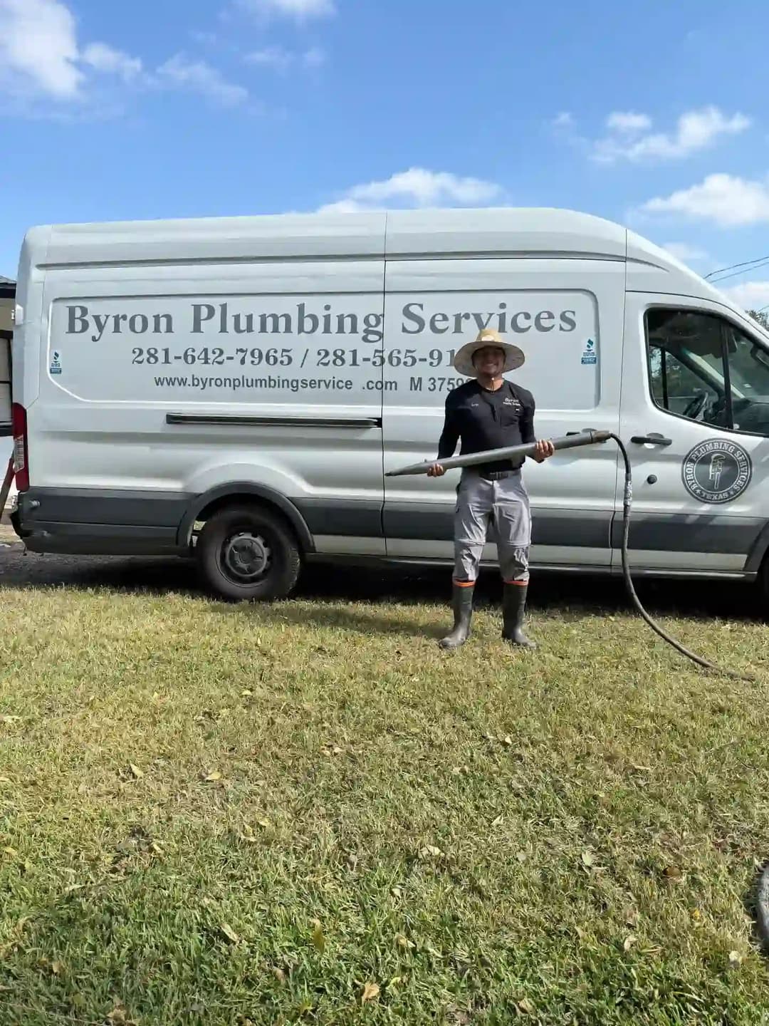 Plumber holding a hose next to a Byron Plumbing Services van in a grassy area.