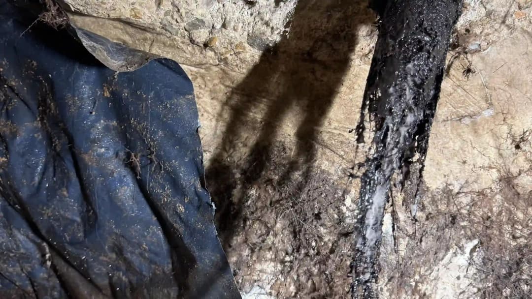 Underground excavation showing dark fabric, dirt, and mineral deposits on rocky surface.