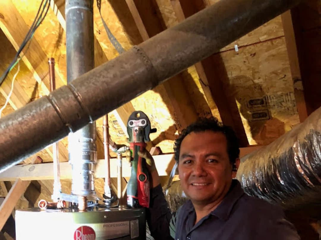 Technician servicing a water heater in an attic, using tools and equipment for maintenance.
